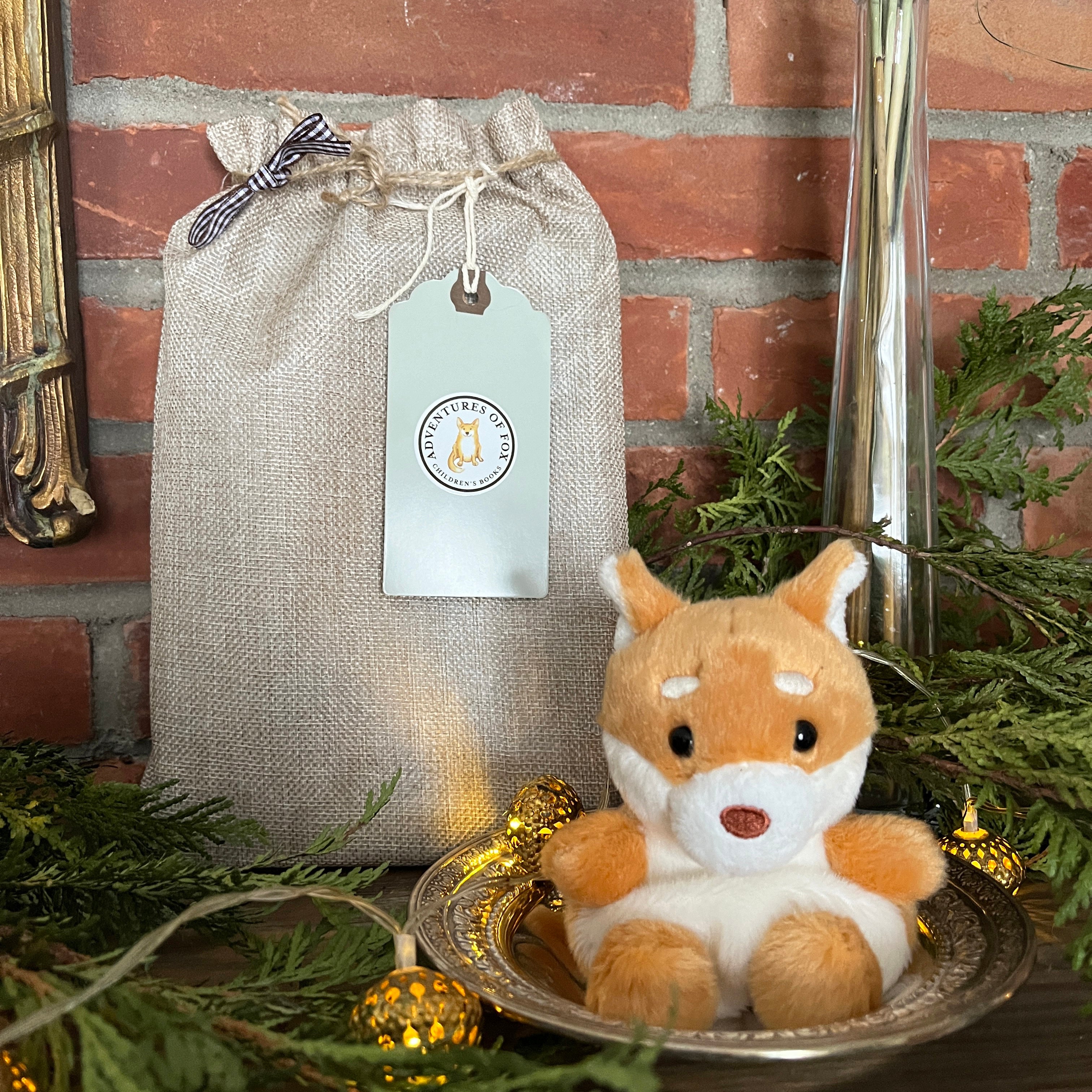 Plush Fox the dog toy next to a gift bag with a tag on a brick wall background